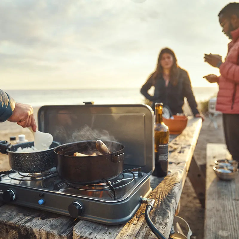 People cooking outdoors on a camping stove with a scenic background