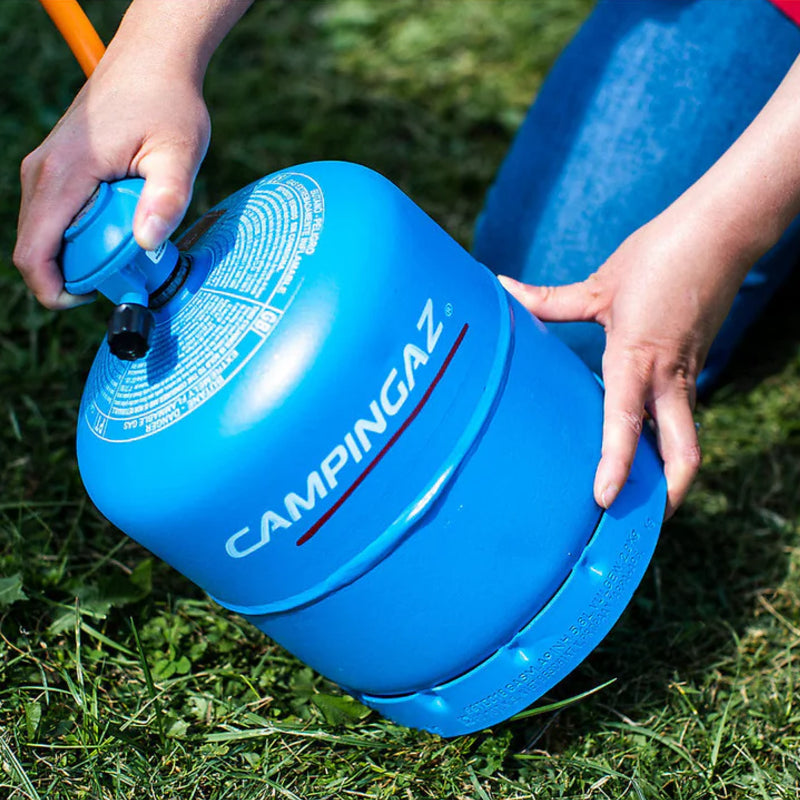 Blue Campingaz fuel canister held by a person on grass