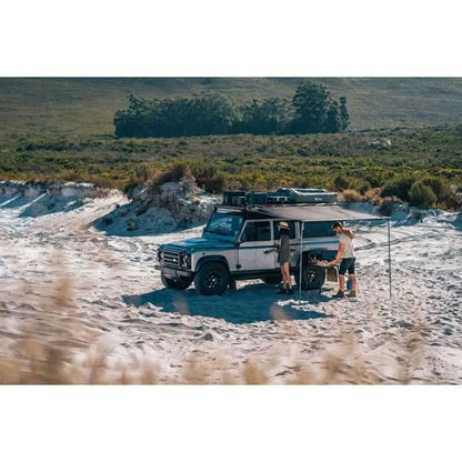 Two people standing next to a Land Rover Defender in a desert-like environment.