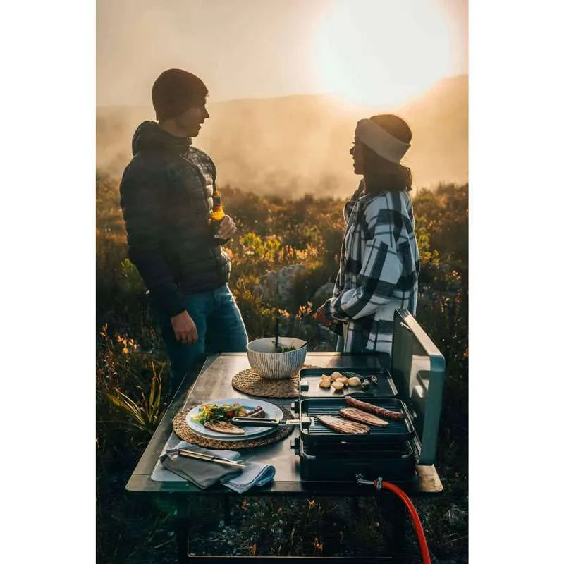 Two people enjoying a meal outdoors on a Cadac camping stove with a scenic background