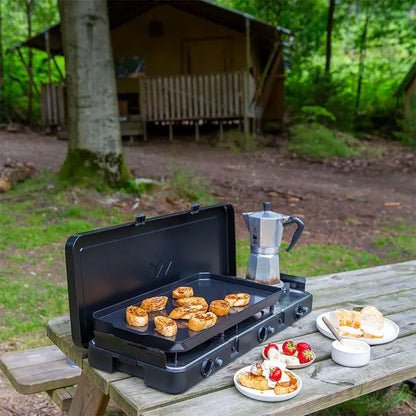 Portable grill with food on a wooden table in a forest setting