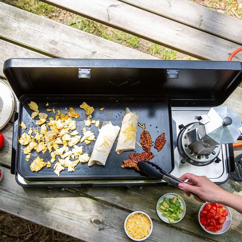 Person cooking on a portable stove with food items on a wooden surface