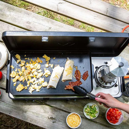 Person cooking on a portable stove with food items on a wooden surface